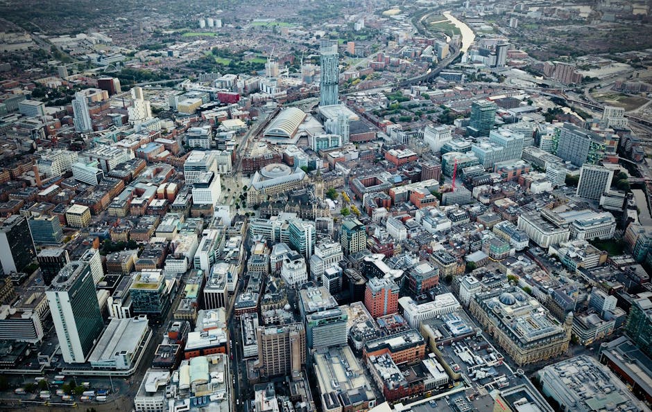 A cityscape featuring a mix of modern and historic buildings under a clear blue sky. In the foreground, there are residential flats with sloped grey roofs and brick facades, some with small windows. B