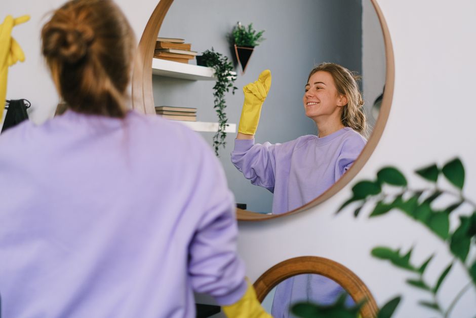 Two professional cleaning specialists from Mike's Cleaners are performing surface cleaning in a modern living room, vacuuming the light grey tiled floor. The room features a sleek, dark grey sofa with
